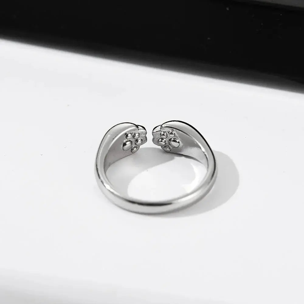 Bague Chat Ouverte et Réglable pour Femme posée sur une table blanche avec un fond noir au dessus
