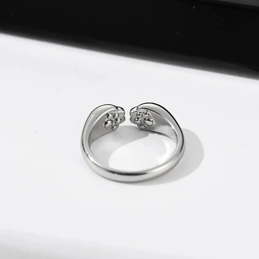 Bague Chat Ouverte et Réglable pour Femme posée sur une table blanche avec un fond noir au dessus