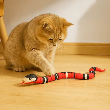 Jouet pour Chat - Serpent Interactif un chat roux devant pied de meuble en bois marron à gauche, joue avec sa patte avant droite avec le serpent sur le sol beige