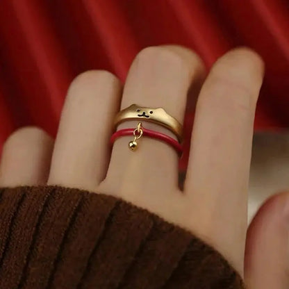 Lot de Deux Bagues Chat Dorées avec Clochette autour du doigt d'une femme avec un pull marron sur fond rouge et blanc