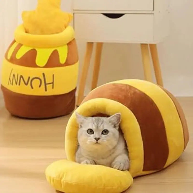 niche chat coussin lit  jolivase une niche au sol avec un chat dedans, une autre niche debout contre le mur et près d'un meuble blanc à quatre pieds en bois